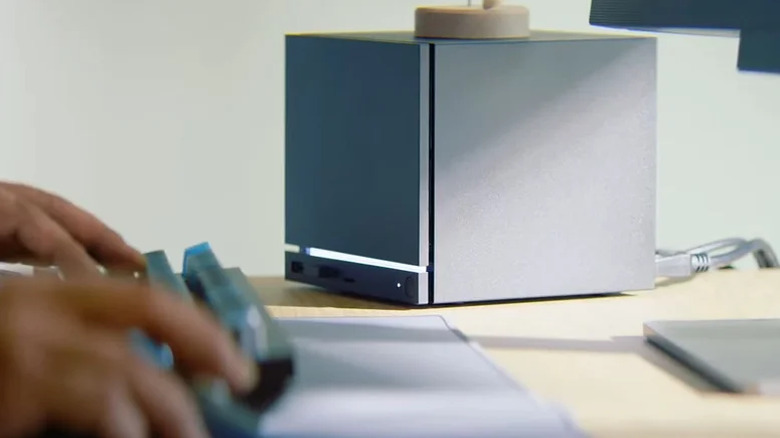 A black Steam Machine from Valve sits on a user's desk, the user's hands can be seen resting on a black keyboard