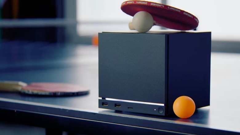 A black Steam Machine with an illuminated white light sits on a ping-pong table among paddles and balls