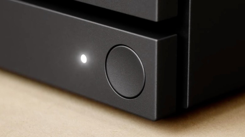 A closeup of the power button on a black Steam Machine, there's also a white indicator light illuminating from the device