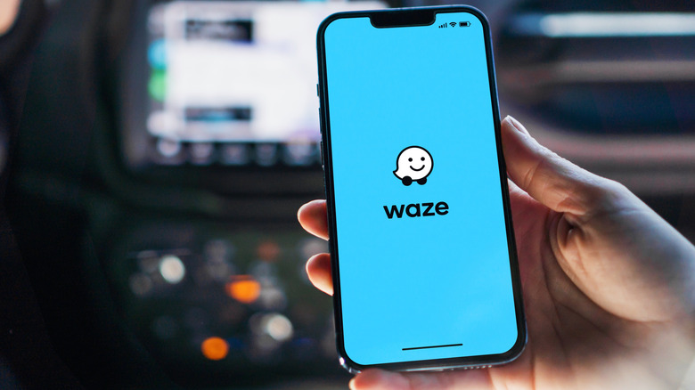 person holding a smartphone showing the Waze loading screen inside a car
