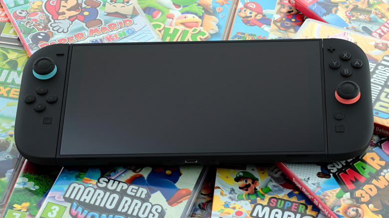 A black Nintendo Switch 2 sits on top a pile of game cases, the screen is turned off on the system