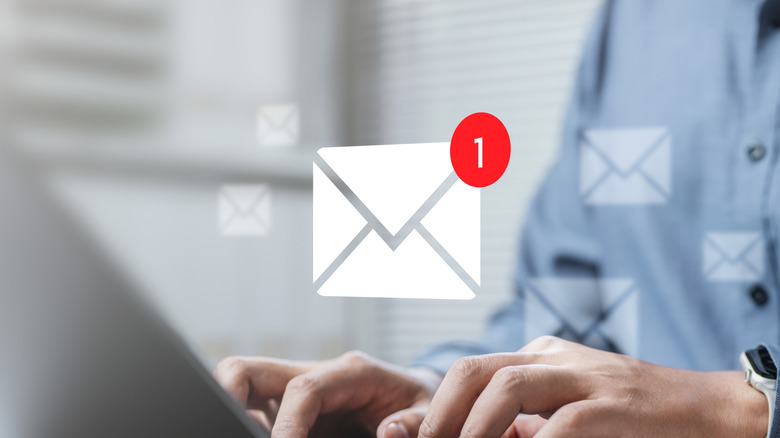 A person using a laptop to check emails with a large email icon in the air surrounded by other, smaller email icons