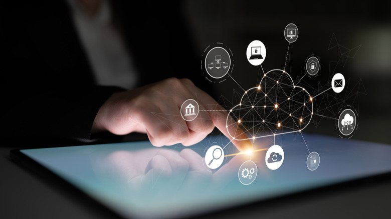 A person tapping on his digital tablet with an icon of cloud storage in the air