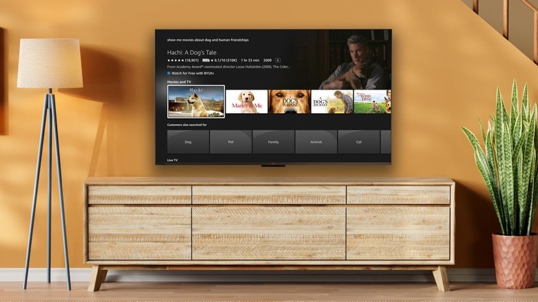An Amazon Fire TV displaying a title card for the movie "Hachi: A Dog's Tale," the TV is a nice room against a brown staircase, a plant and a lamp are next to it