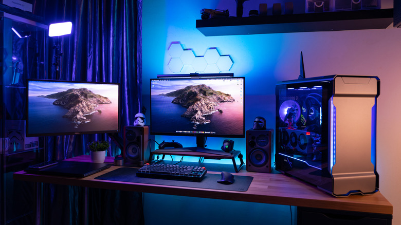 RGB-lit desktop gaming setup with dual monitors, speakers, keyboard, mouse, and a glass PC case