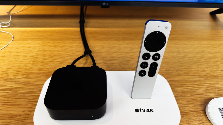 apple tv 4k sitting on stand with its remote on a wooden table with cables running to an LG tv at the back