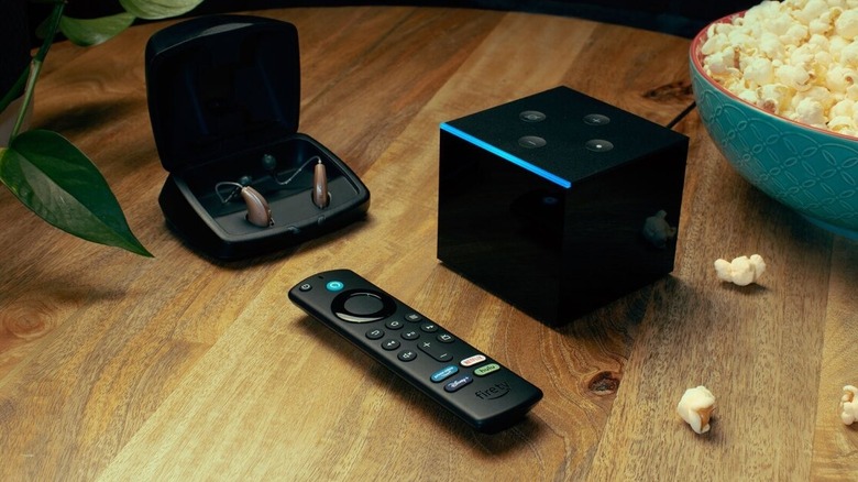 A Fire TV remote next to a Fire TV Cube, earphones, and popcorn on table