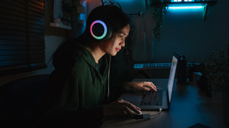 A woman playing a video game on a laptop with flashy headphones on