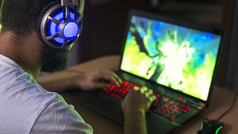 A man playing a game on a gaming laptop while wearing flashy headphones