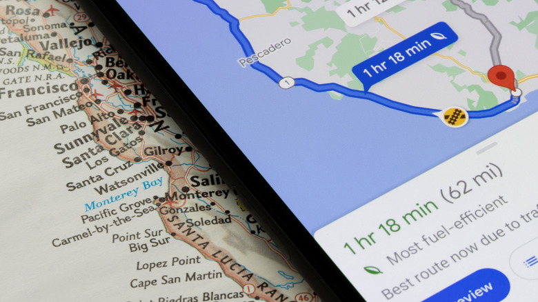 A smartphone sitting on a map of California displays a Google Maps route that shows a fuel-efficient way to travel the coast of California