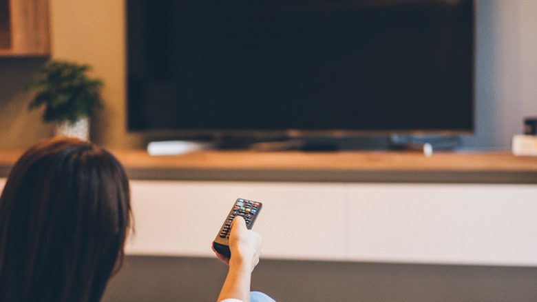 Woman pointing remote at black TV screen