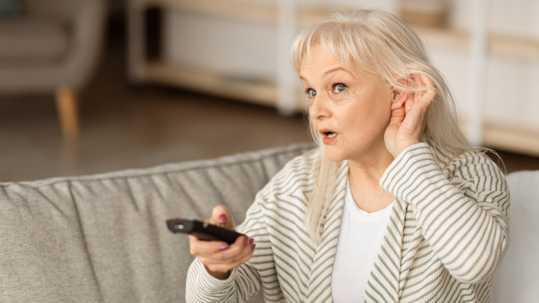 Old woman having a hard time hearing TV while holding remote