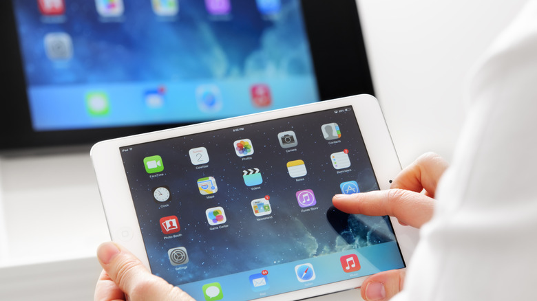 White iPad held in hand in front of bigger monitor