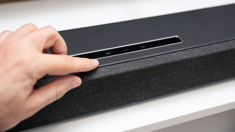 person operating the touch controls on a soundbar placed on white table