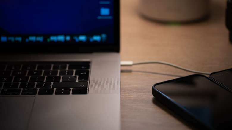 A laptop connected to a smartphone via a charging cable