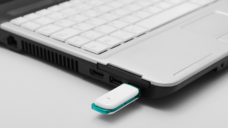 Close-up a white and teal USB flash drive plugged into a silver laptop with white keyboard.