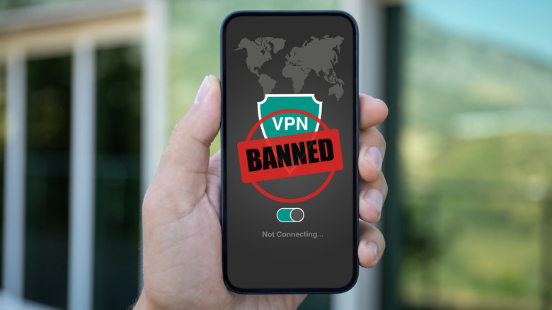 person holds a smartphone with an active VPN app and a banned icon on top