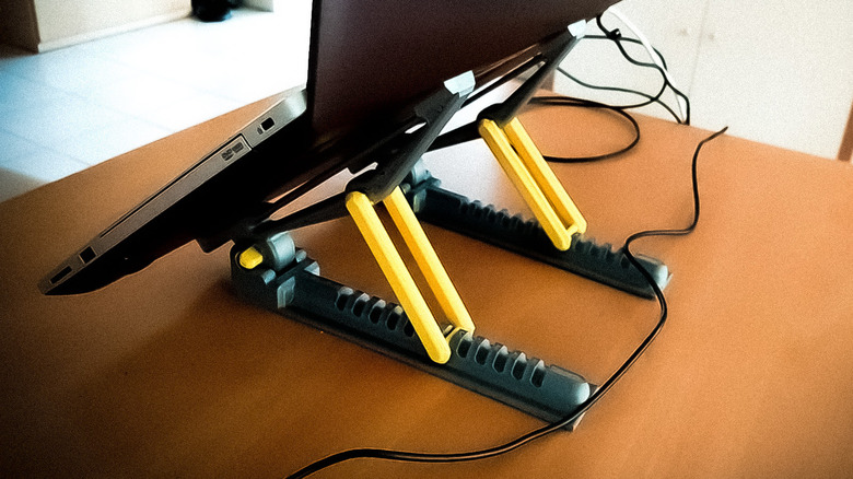Repositionable laptop stand holding up a laptop on a wood table