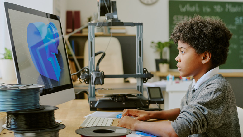 A boy working at a computer beside a 3D printer
