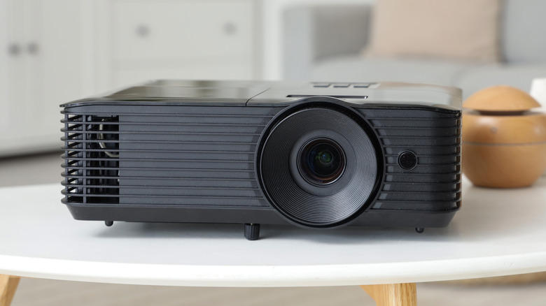 A black projector faces the camera as it sits on a white table