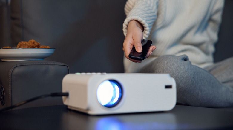 An individual in a white sweater holds a black remote control near a projector