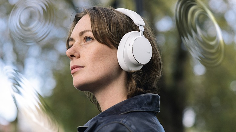 A pair of white AKG N9 Hybrid Noise Cancelling Headphones as worn by an individual who is standing outside, surrounded by three computer-generated soundwaves