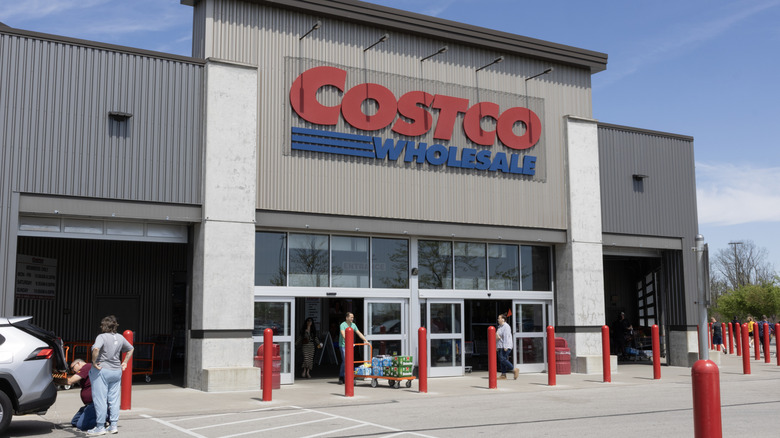The front exterior of a Costco Wholesale Retail Store, several shoppers can be seen entering and exiting the store