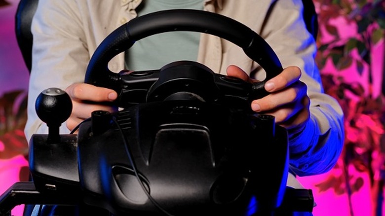 An individual in a light gray jacket with both of their hands on a racing wheel for video games