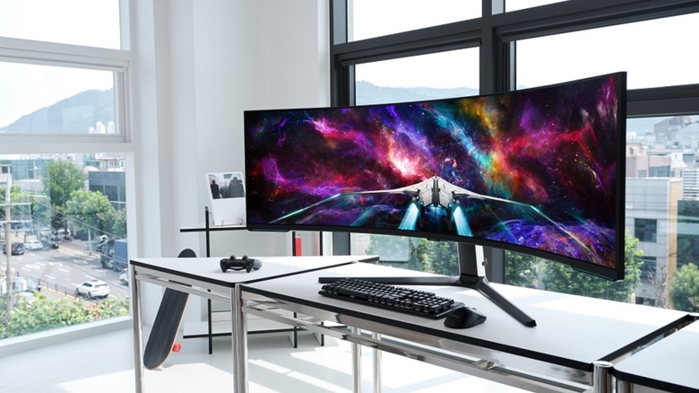 A Samsung promotional photo for the 57-inch Odyssey Neo G9 Series Curved Gaming Monitor, the monitor sits on a desk in a white room with ample windows