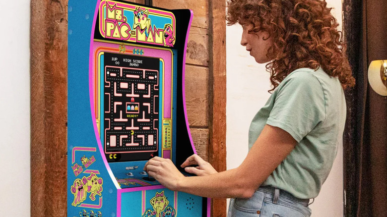 A promotional image for the Arcade1Up "Ms. Pack-Man" Partcade, the image depicts the "Ms. Pac-Man" arcade game and aesthetics that adorn the machine