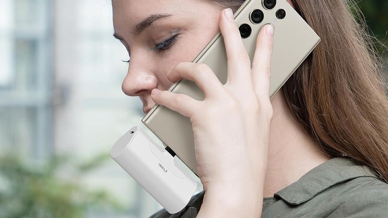 A woman talking on a phone with an iWalk portable charger plugged in.