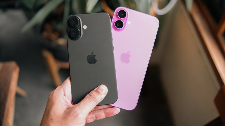 A closeup of an individuals' left hand holding a black iPhone and a pink iPhone