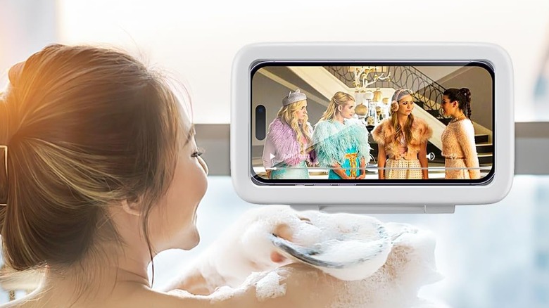 An individual is watching a television show on their iPhone that is encased in the LC-dolida Waterproof Shower Phone Holder, the individual is in the tub and applying soap to their upper shoulder