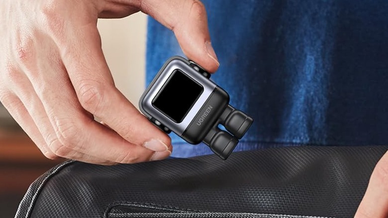 An individual's right hand holds the UGreen Uno 30W USB-C Charger Block as they prepare to put it in their black bag