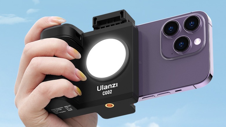 An iPhone is attached to the UURig CG-02 Grip Holder, which is being held in an individuals' right hand against a mostly cloudless sky