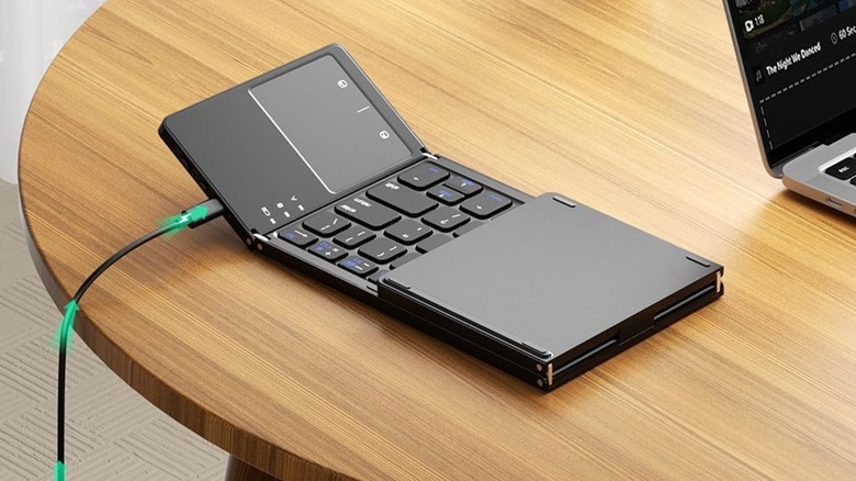 The Samsers Foldable Bluetooth Keyboard sitting on a brown table next to an MacBook that's mostly cropped from the photo due to it being in the corner