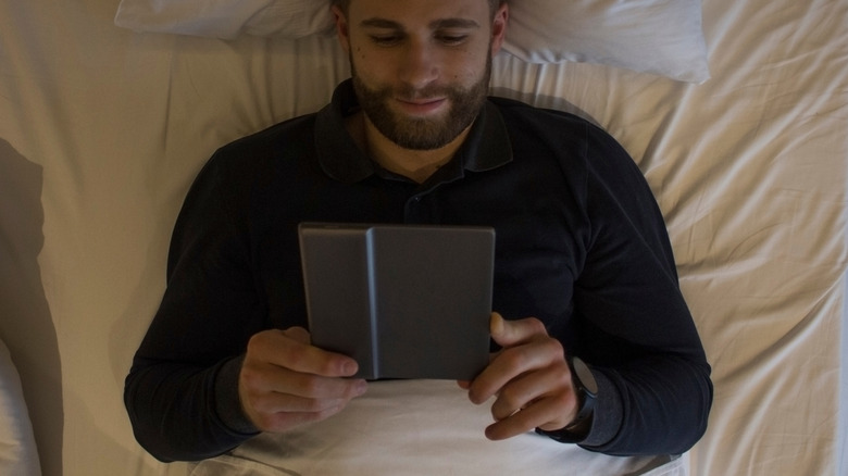 A man reading an e-reader in bed