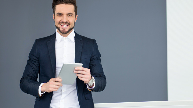 A man in a suit holding an e-reader and smiling