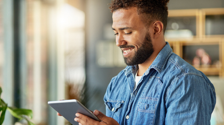 A man smiling and reading on an e-reader