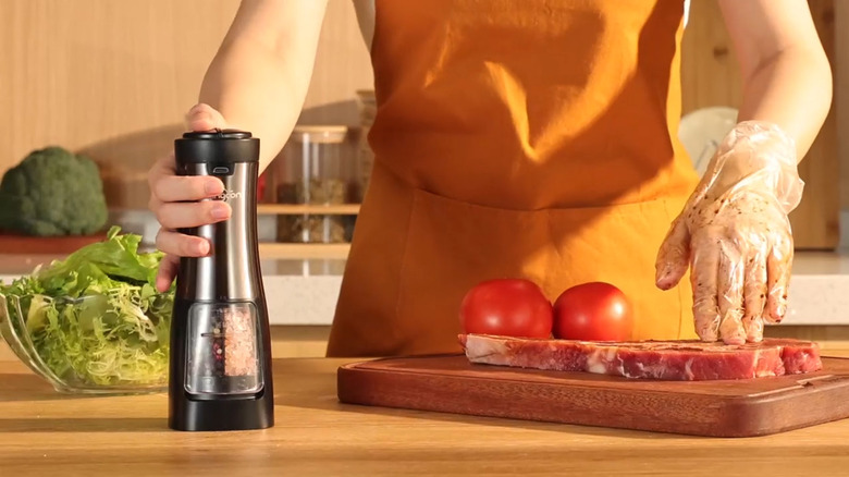Hand holding Sangcon 2-in-1 Electric Salt and Pepper Grinder while preparing meat in the kitchen