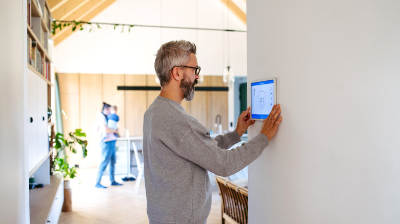 Man adjusting a smart home control panel on a wall.