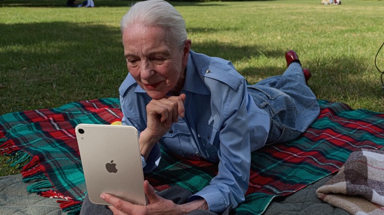 An elder woman using an iPad mini outdoors on a picnic blanket