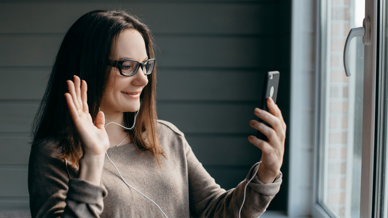 Happy brunette woman in glasses making facetime video call with smartphone at home