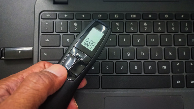 Man holding a wireless presentation laser pointer over a laptop keyboard