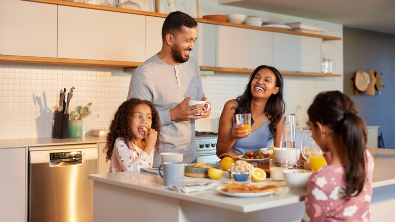 A family of four laughing in the kitchen while eating.