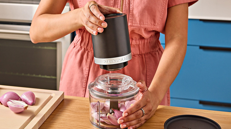 A woman using the KitchenAid Go food chopper to chop red onions.