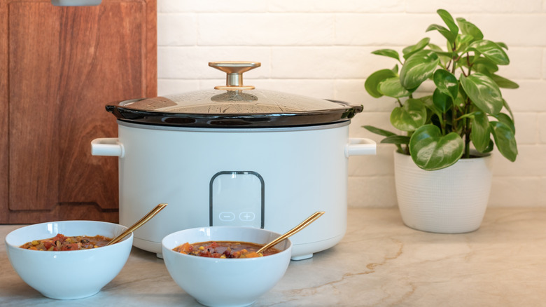 Slow cooker on kitchen counter with two bowls of soup.