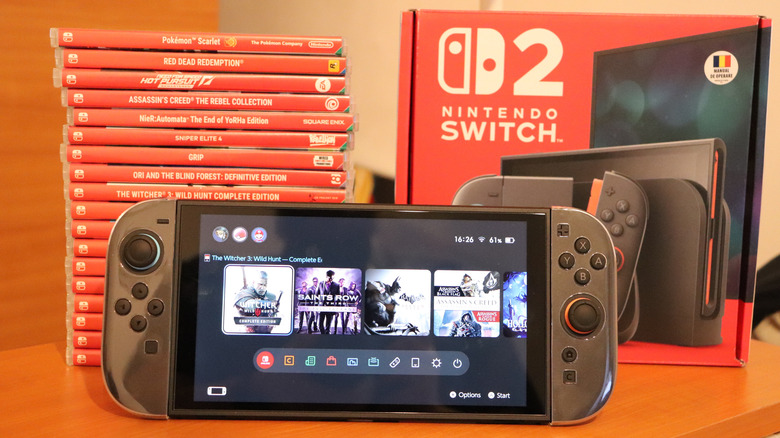 Nintendo Switch 2 console with game library on screen beside stacked game cases and retail box.
