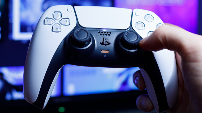 Someone holding a PlayStation 5 controller with their digital game collection on a TV in the background.