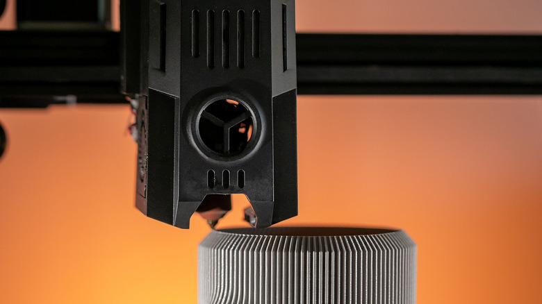 3D print head printing an object on orange background